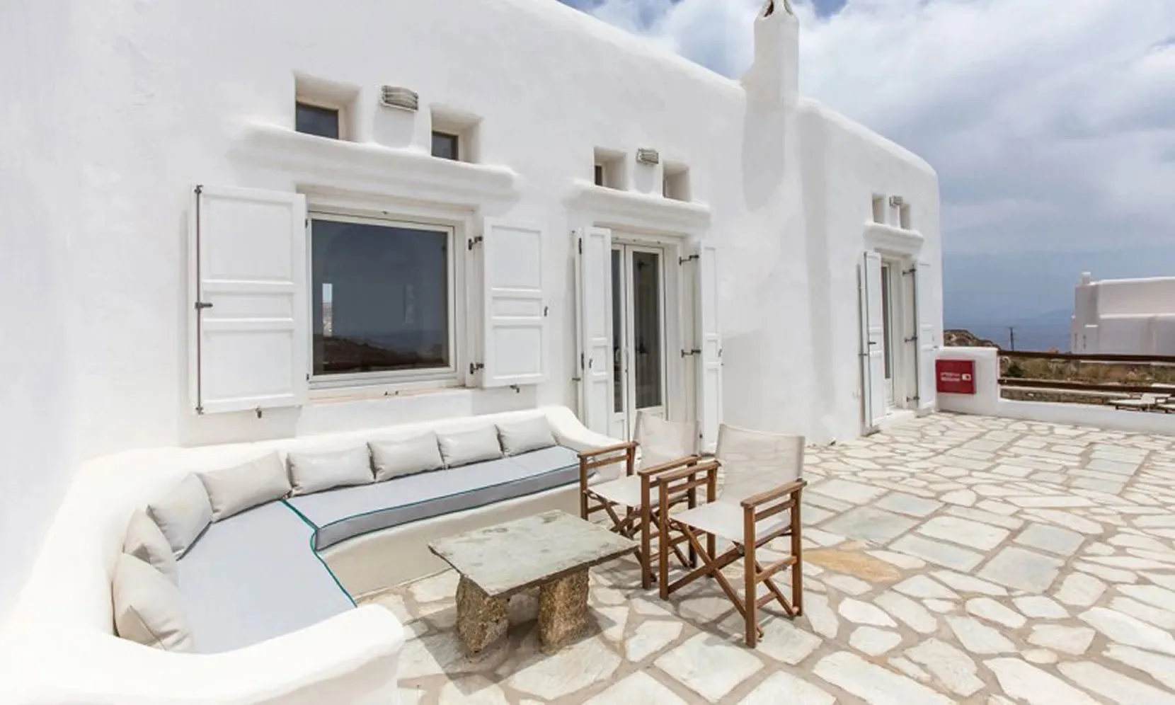 A white outdoor terrace with built-in seating and a stone-paved floor.