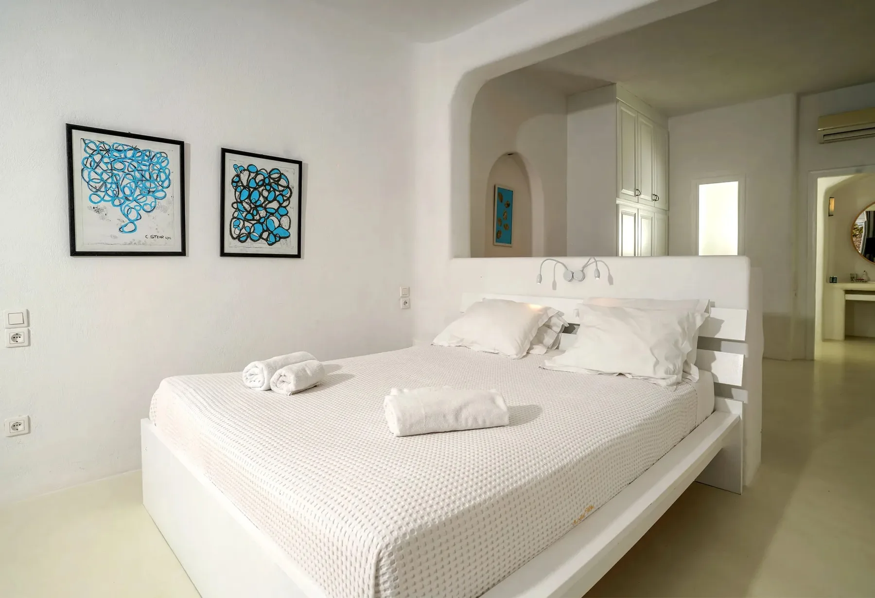 A bright bedroom with a neatly made bed and framed artwork on the wall.