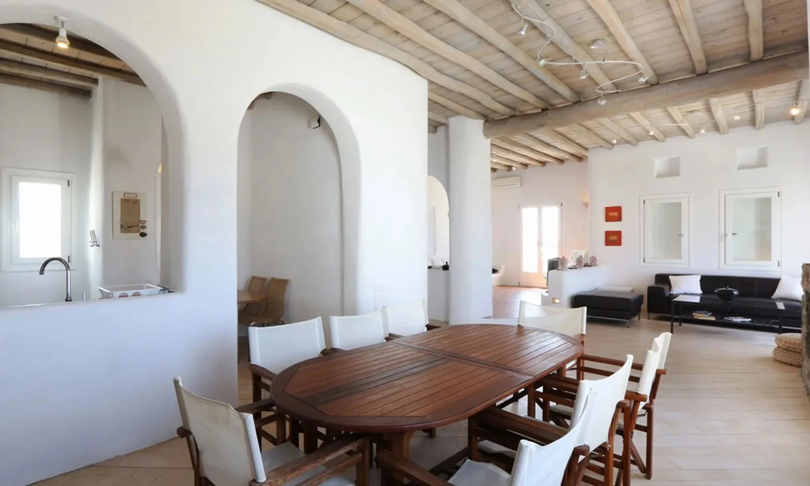 A dining table and seating sit beside an open living area with a wood-beamed ceiling.