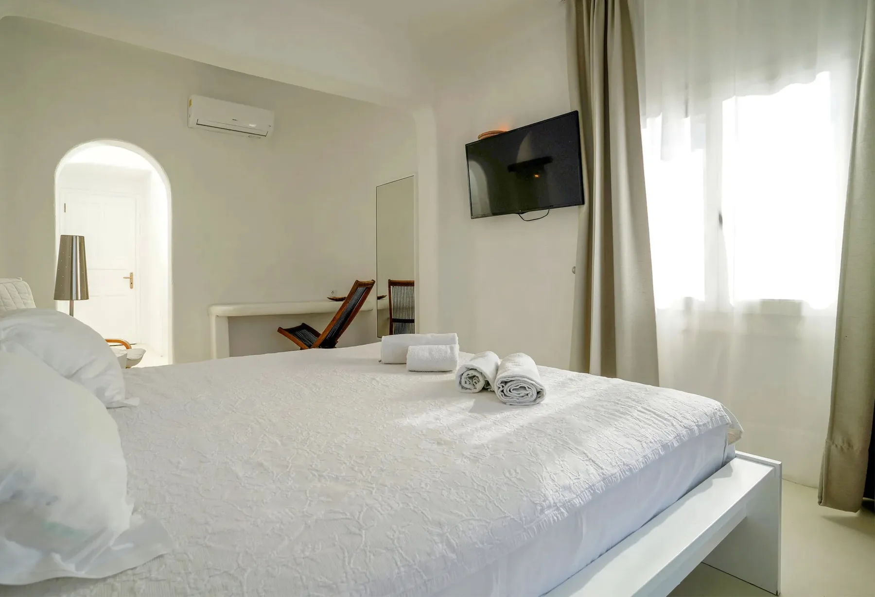 A bedroom with a neatly made bed and a television mounted on the wall.