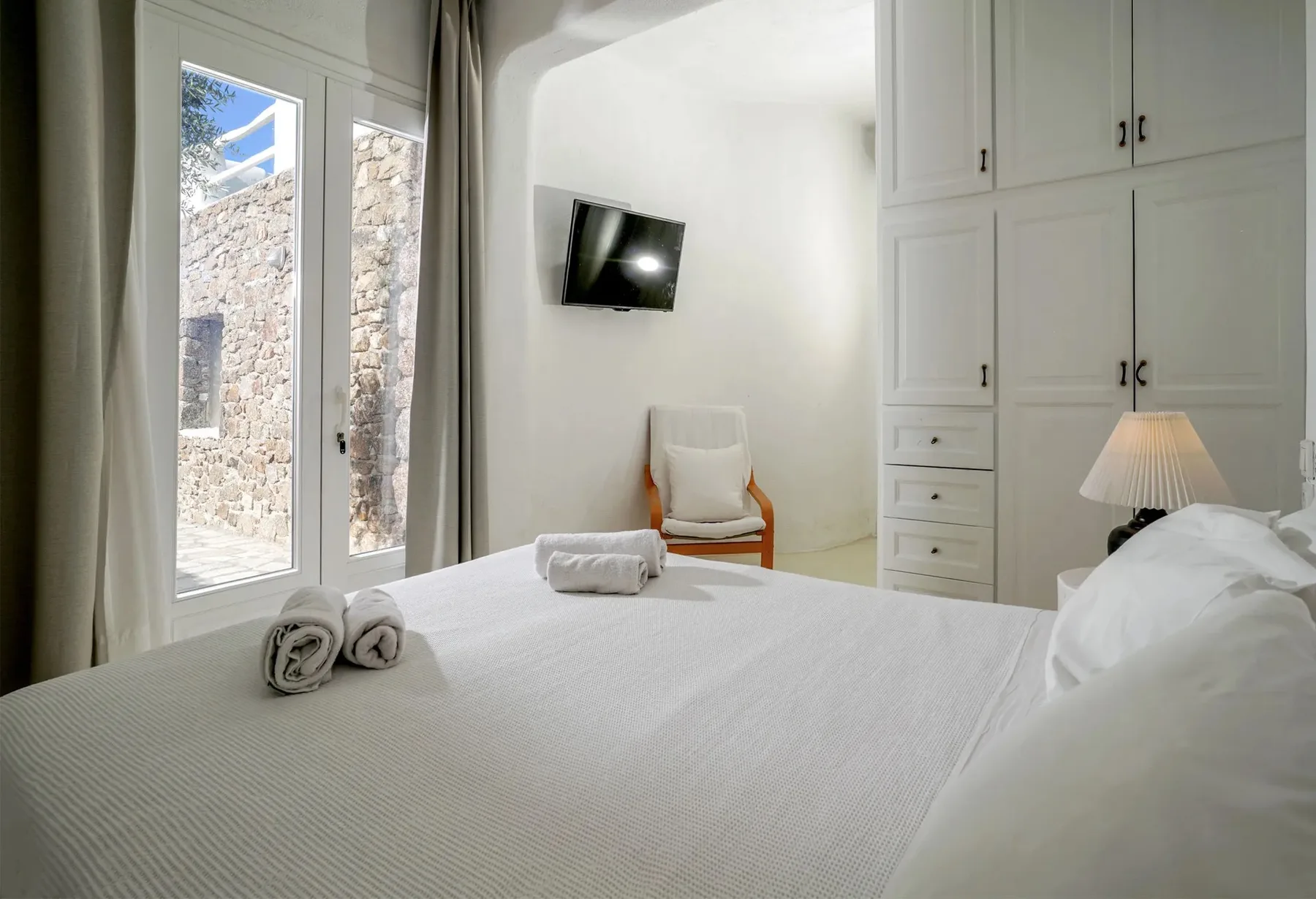 A bright bedroom with a neatly made bed, a chair, and built-in cabinets.
