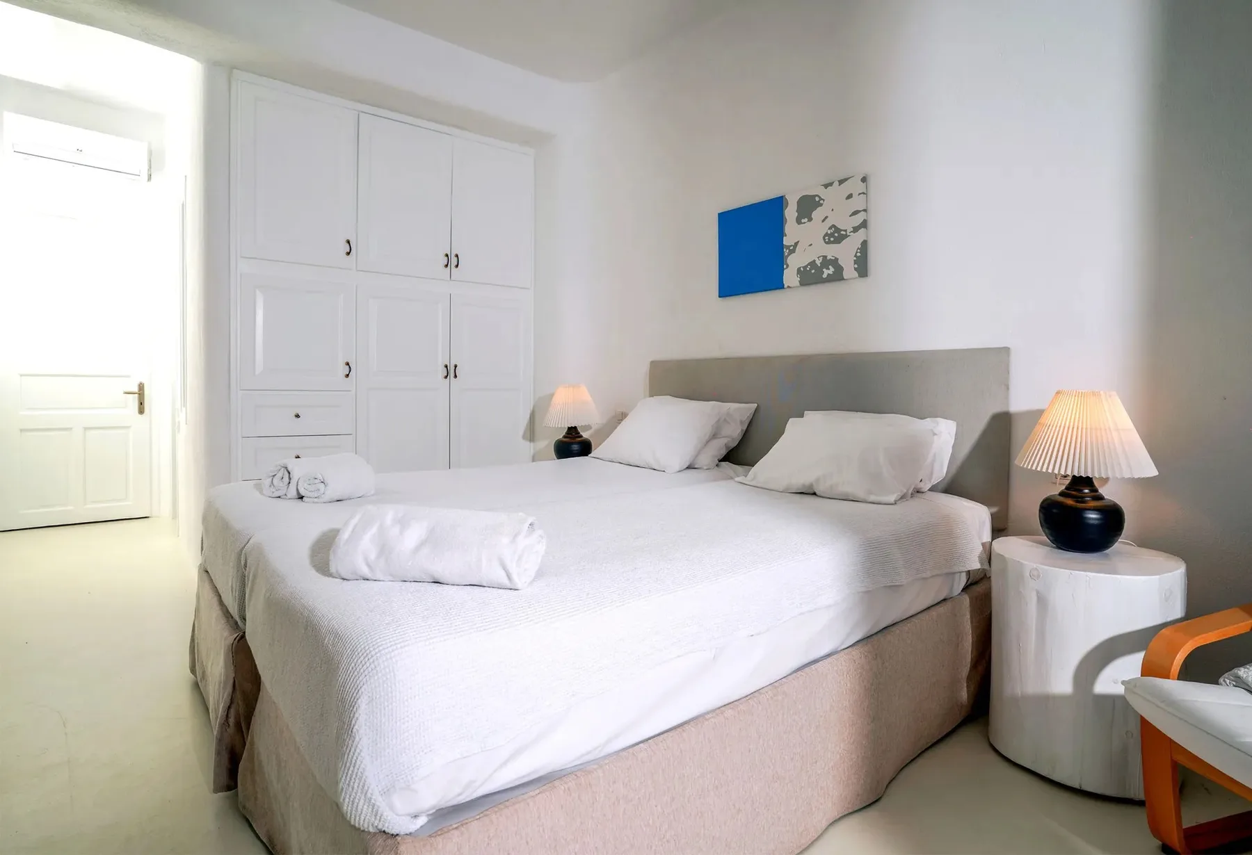 A bright bedroom with a large bed, white bedding, and bedside lamps.