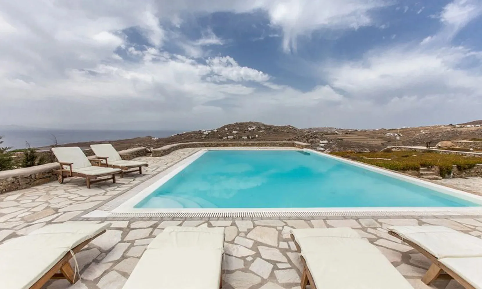 An outdoor swimming pool with sun loungers on a stone-paved terrace.
