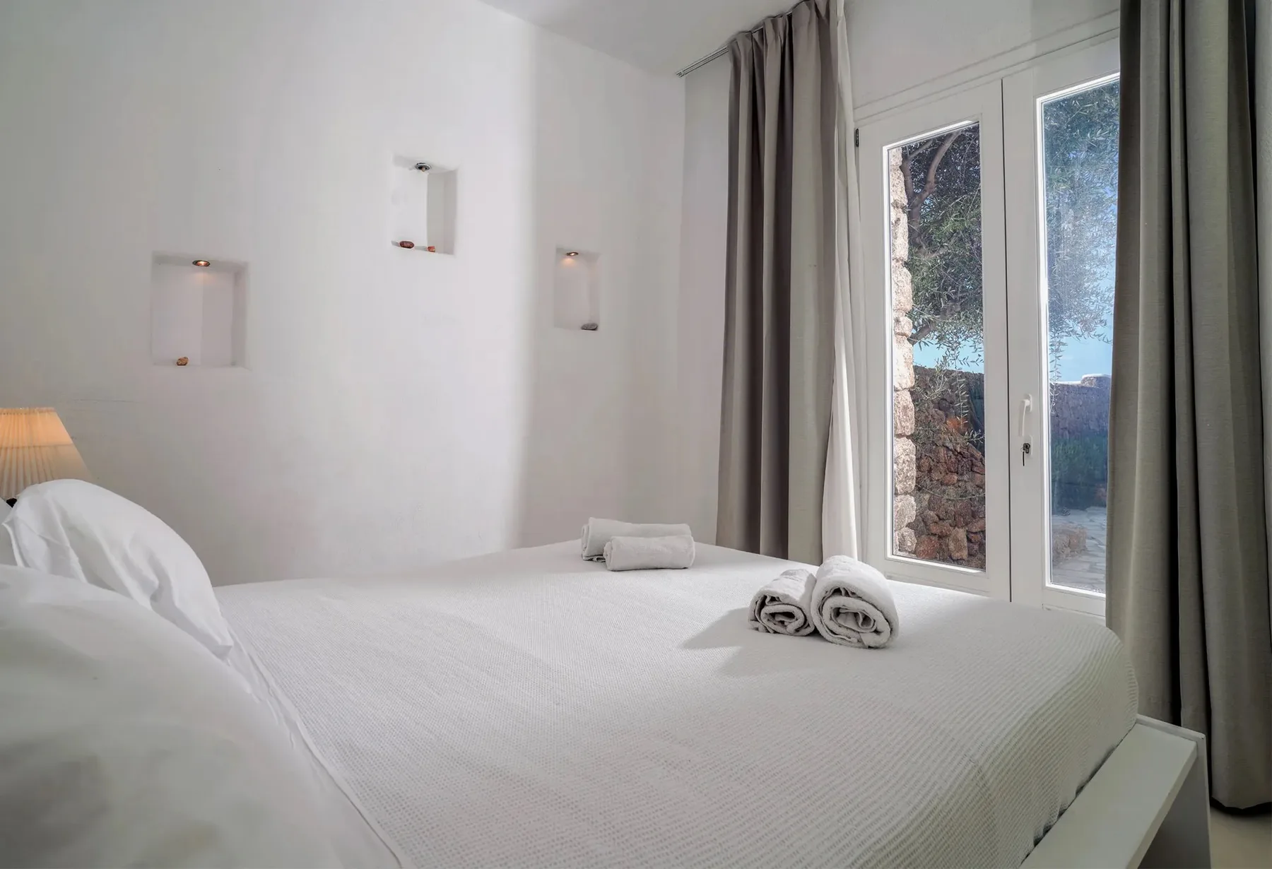 A bright bedroom with white bedding and a curtained glass door.