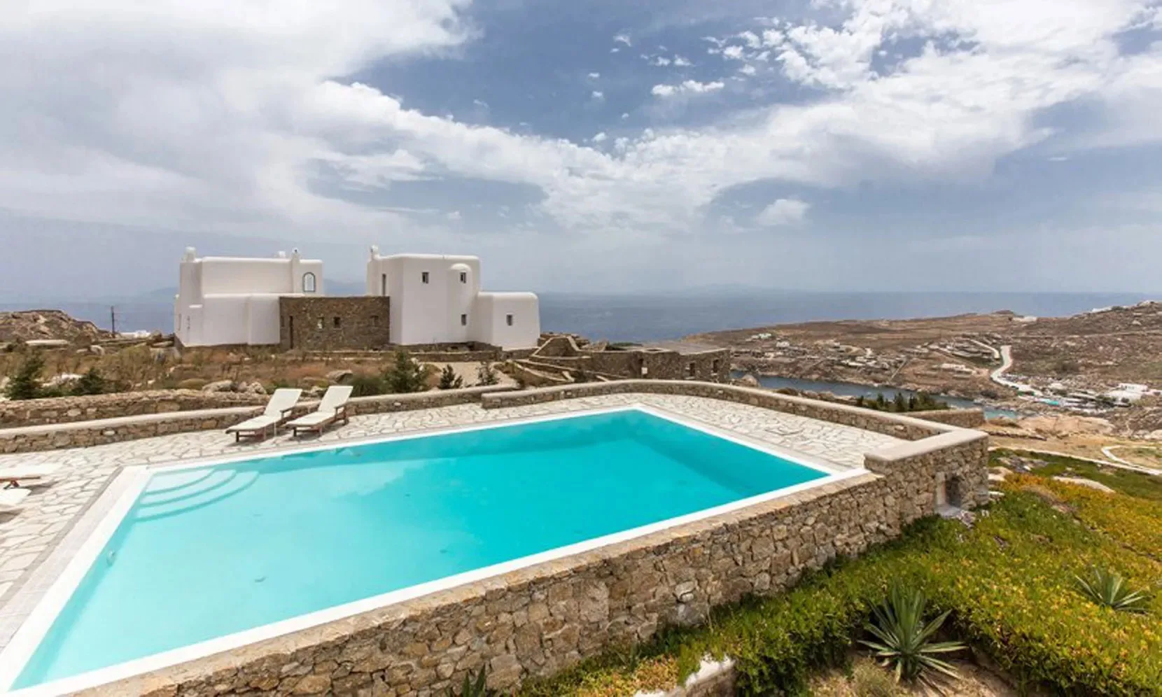An outdoor swimming pool overlooks a dry coastal landscape.