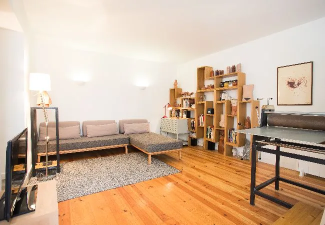 Una sala luminosa con una zona de asientos en esquina y estanterías de madera.