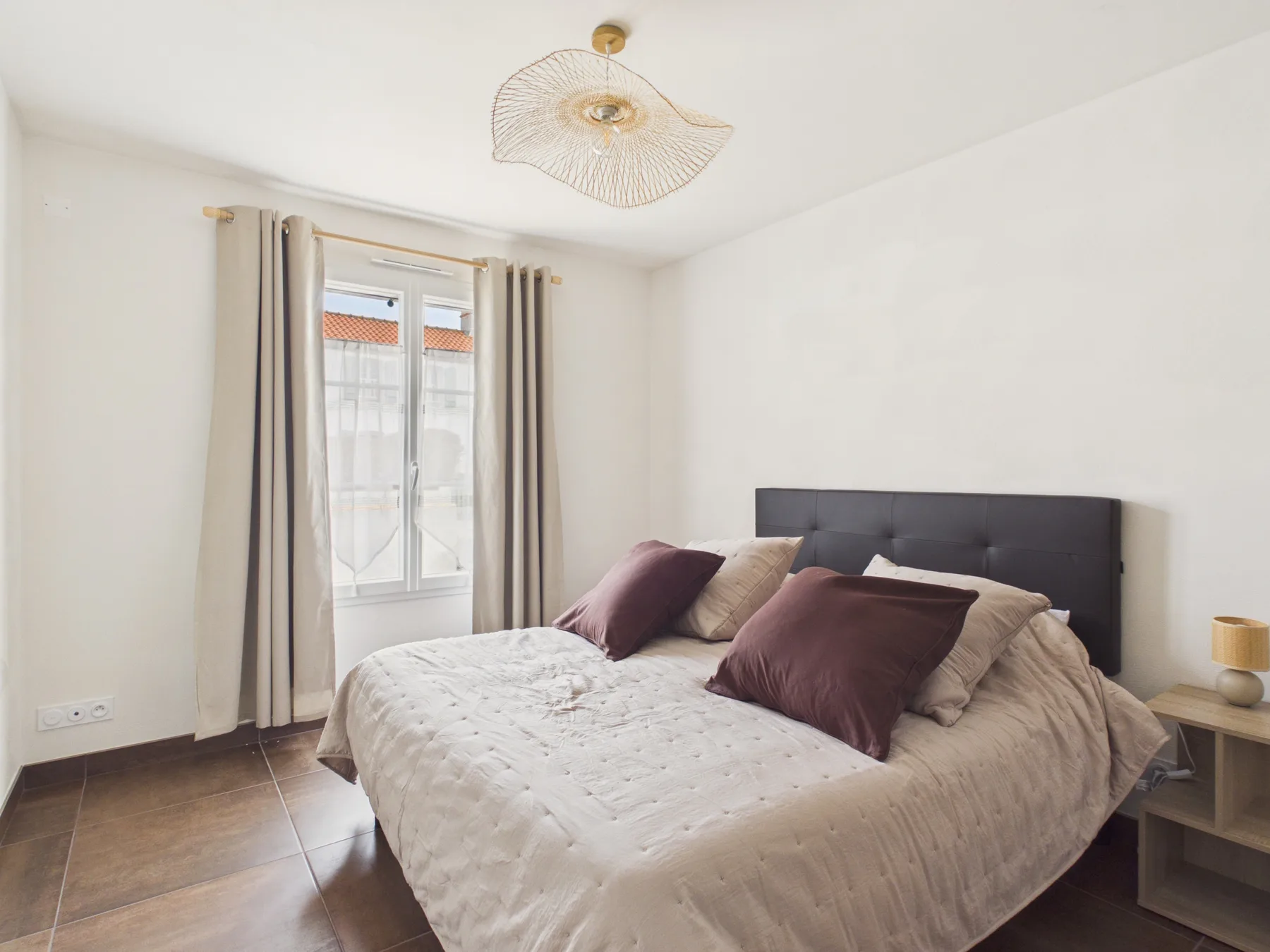 A bright bedroom with a bed beside a curtained window.