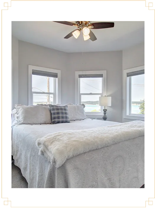 Representative hotel space: A bright bedroom with a bed beneath three windows and a ceiling fan.