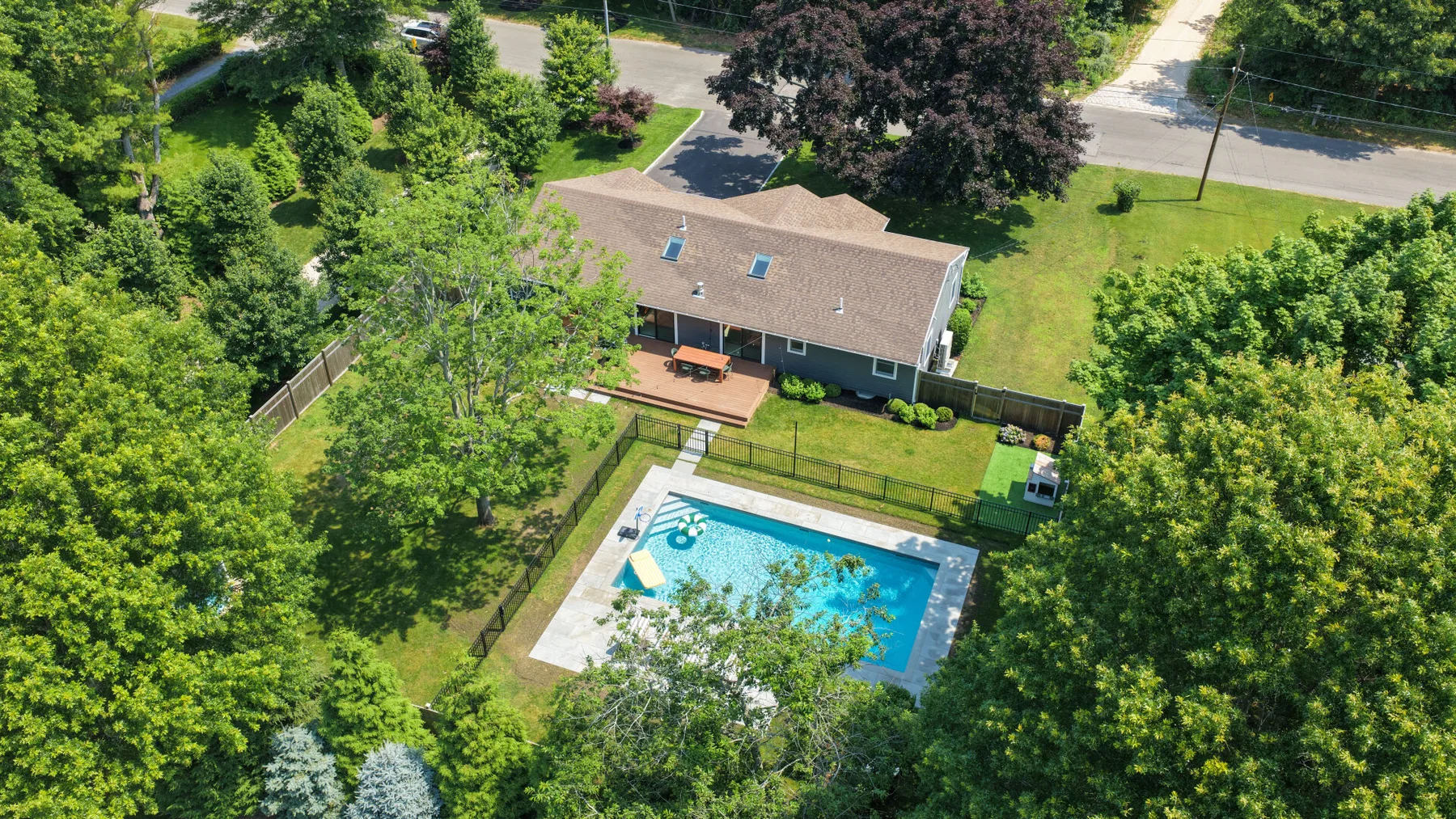 Vista aérea de una casa y una piscina exterior rodeadas de árboles.
