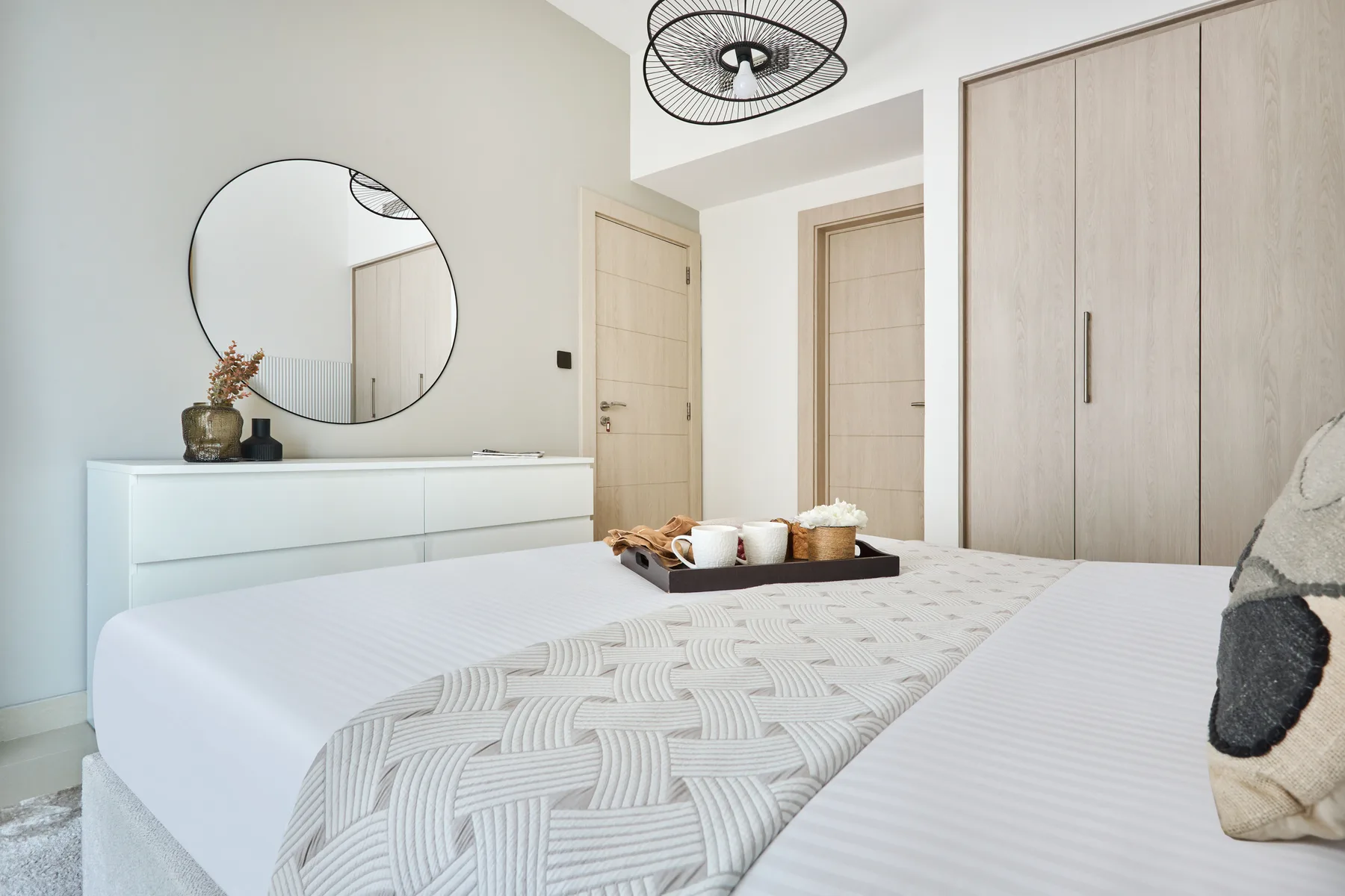 Un dormitorio luminoso con una cama bien tendida y una cómoda blanca.