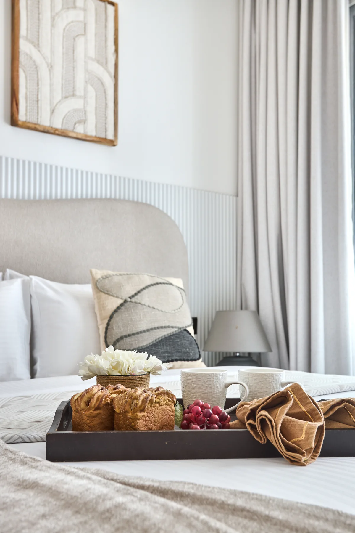 Un dormitorio con una bandeja de desayuno sobre la cama y cortinas junto a la ventana.