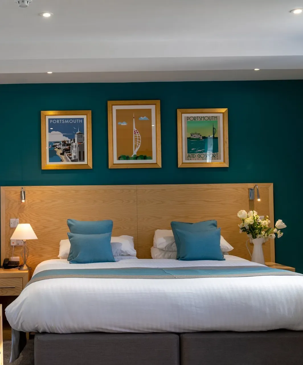 Espacio representativo del hotel: Dormitorio con una cama tendida, cojines turquesa y cuadros enmarcados.