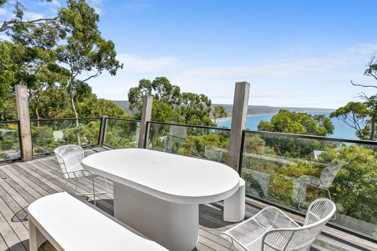 Una terraza exterior tiene una mesa blanca y asientos con vistas a árboles y agua.