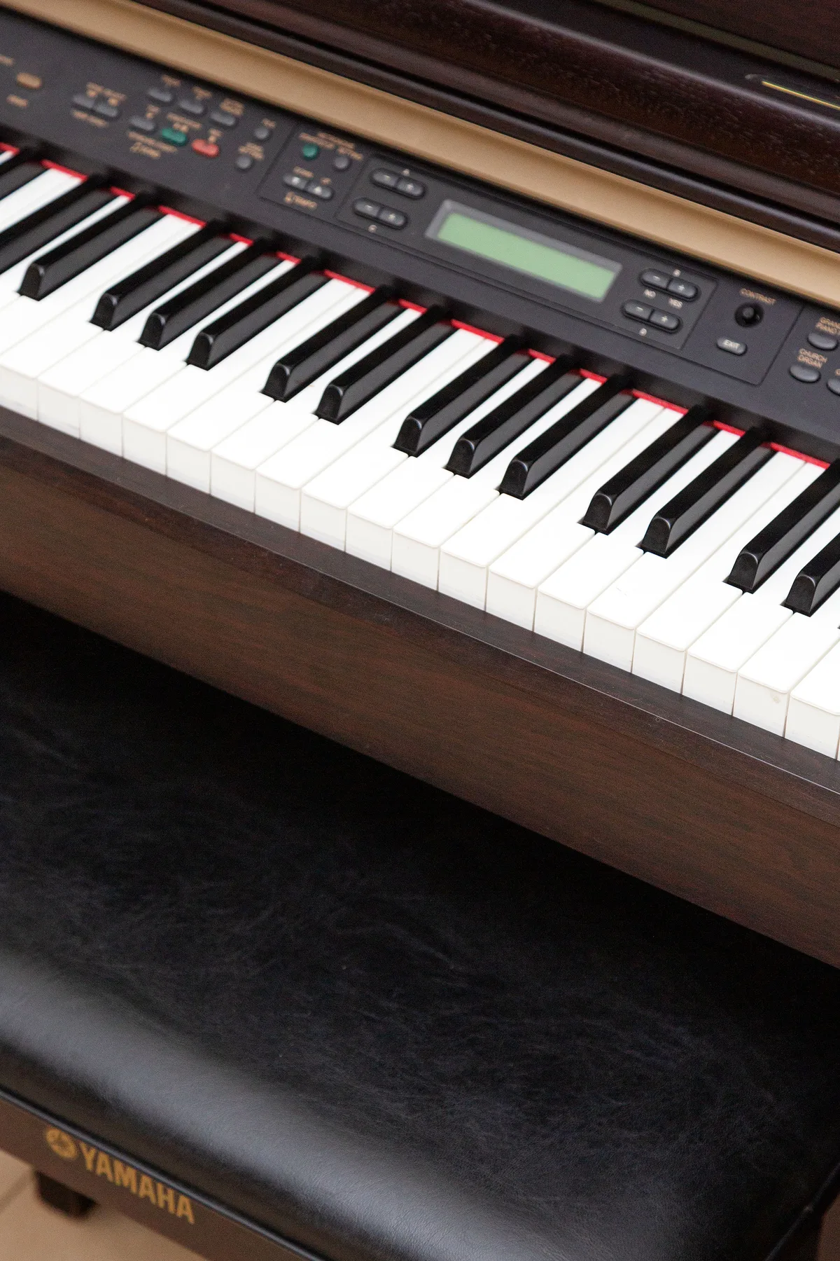 A digital piano keyboard with a display sits above a padded bench.