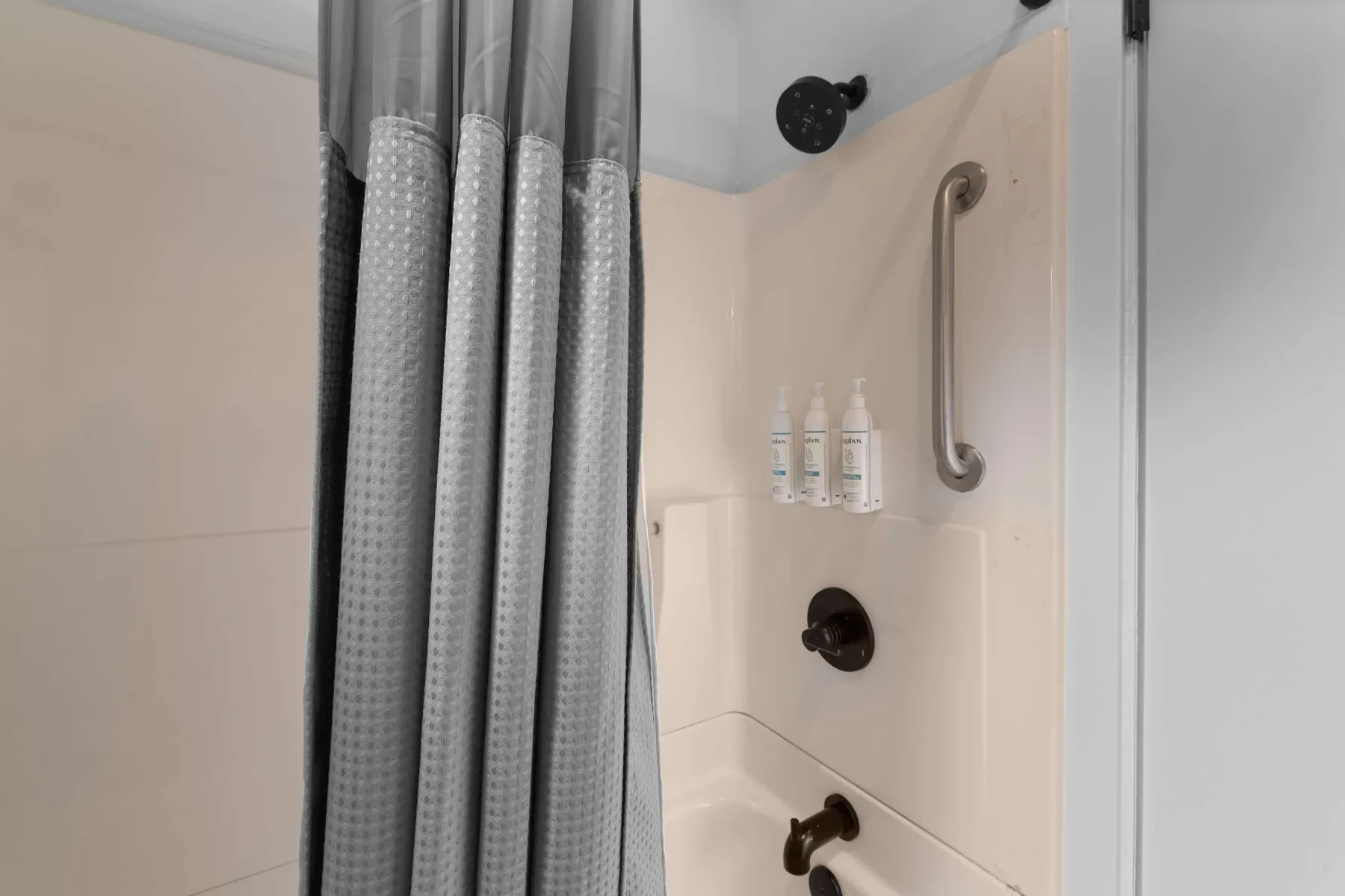 A bathroom shower with a curtain and wall-mounted grab bar.