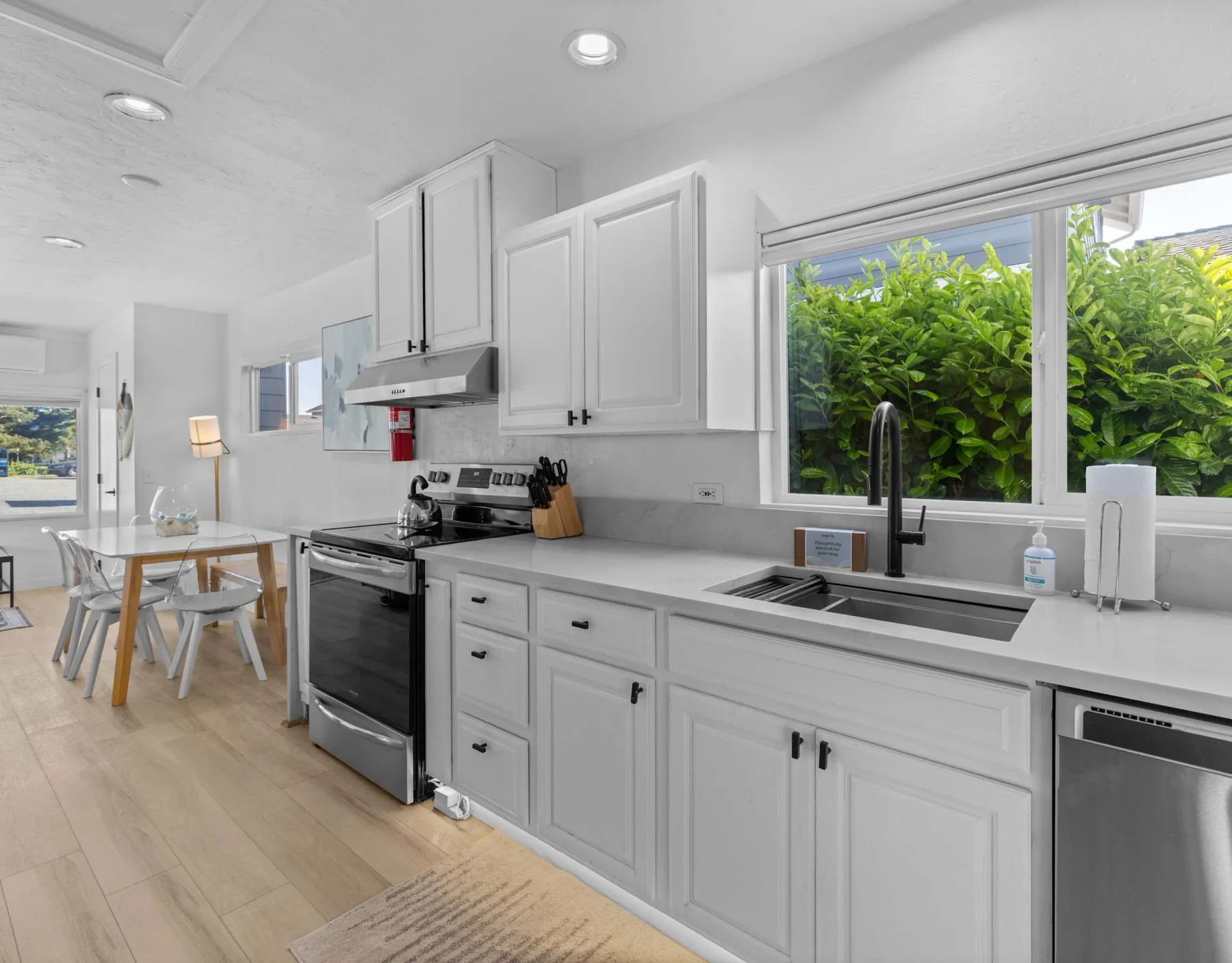A bright kitchen with white cabinetry and a long countertop beneath a window.
