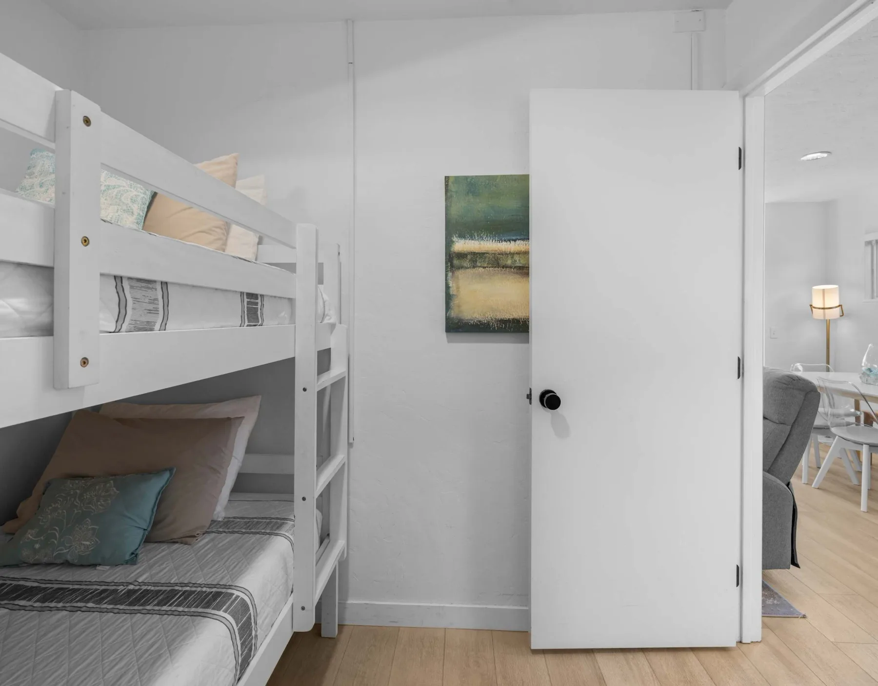 A bedroom with a white bunk bed and an open door to a sitting area.
