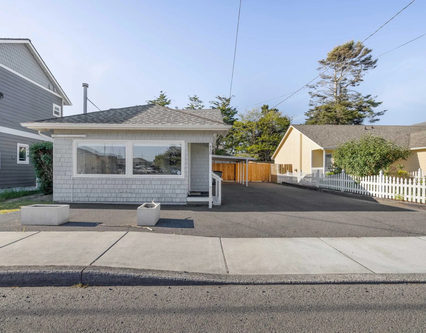 A street-side view shows a gray building beside a paved driveway and neighboring homes.