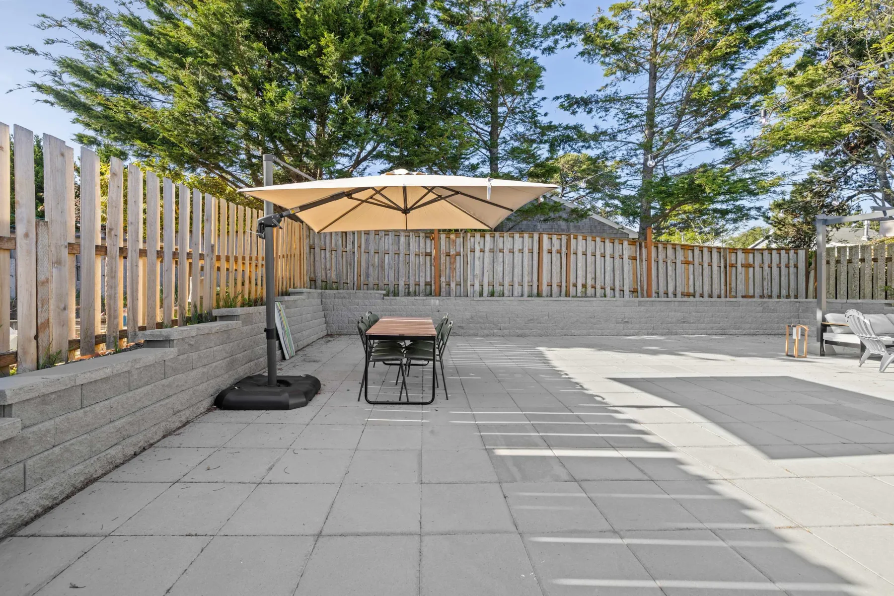 A paved outdoor patio has a table beneath a large umbrella.