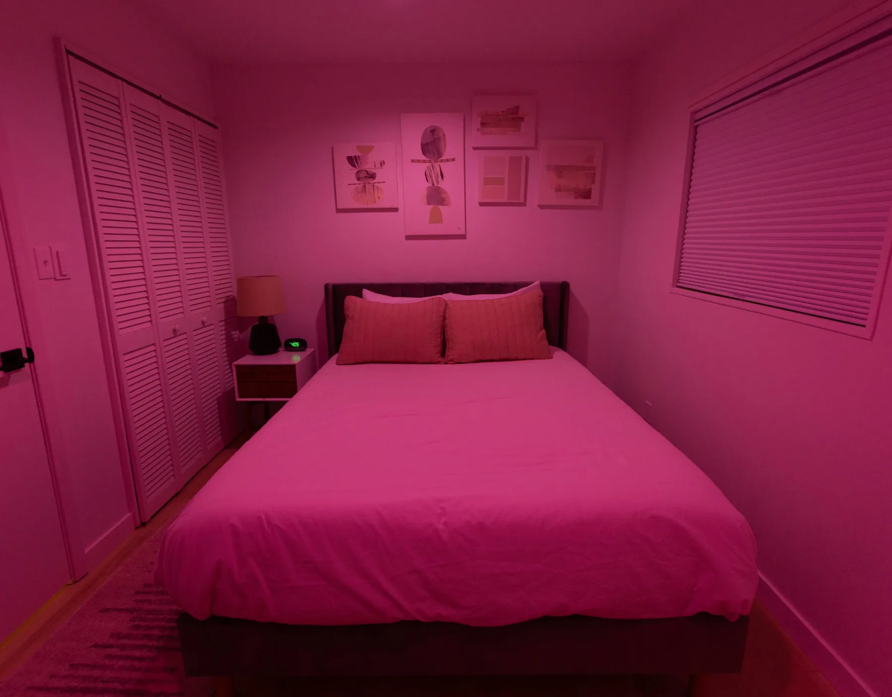 A bedroom with a bed beneath framed artwork and windows on either side.