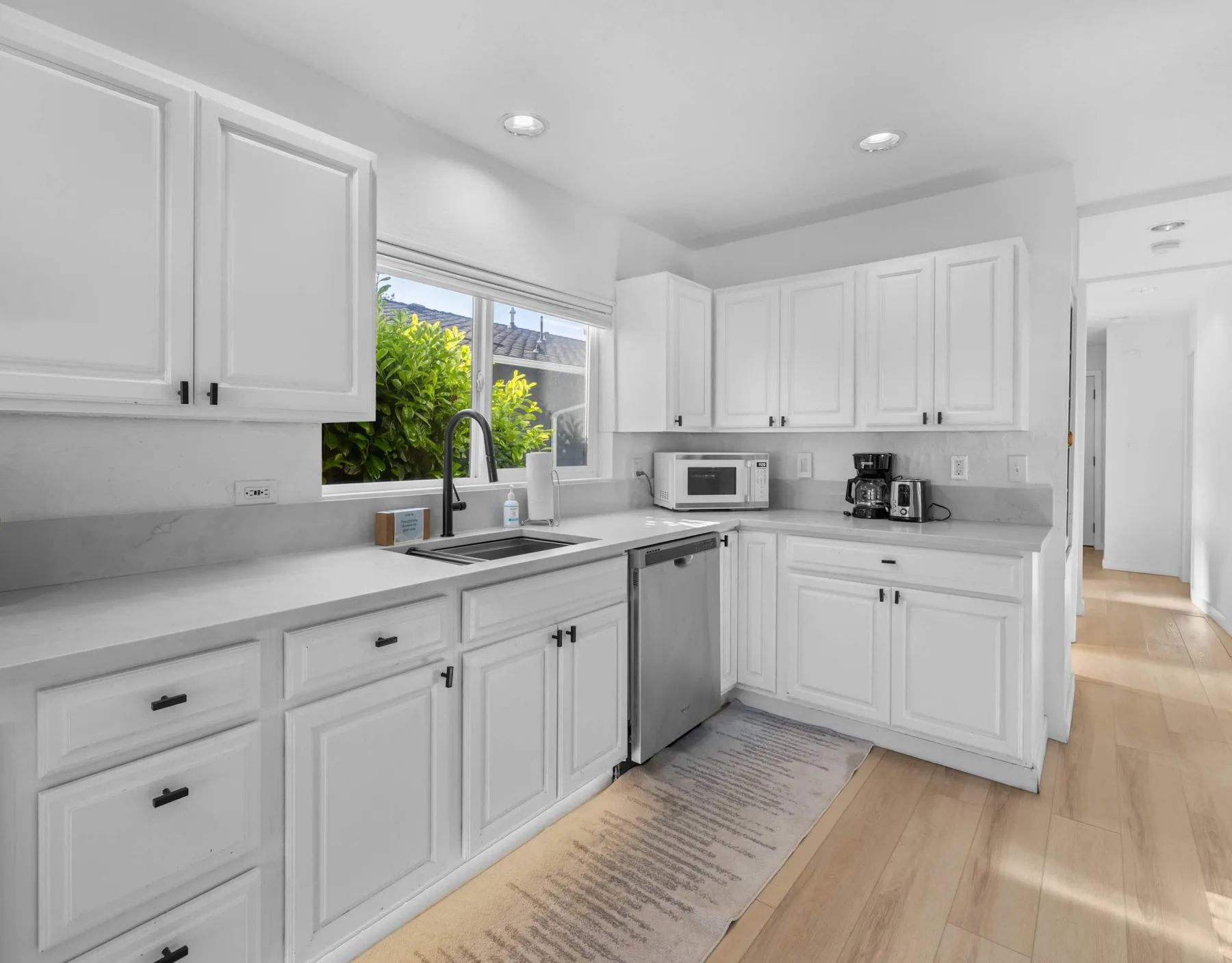 A bright kitchen with white cabinets, a sink, and stainless steel appliances.