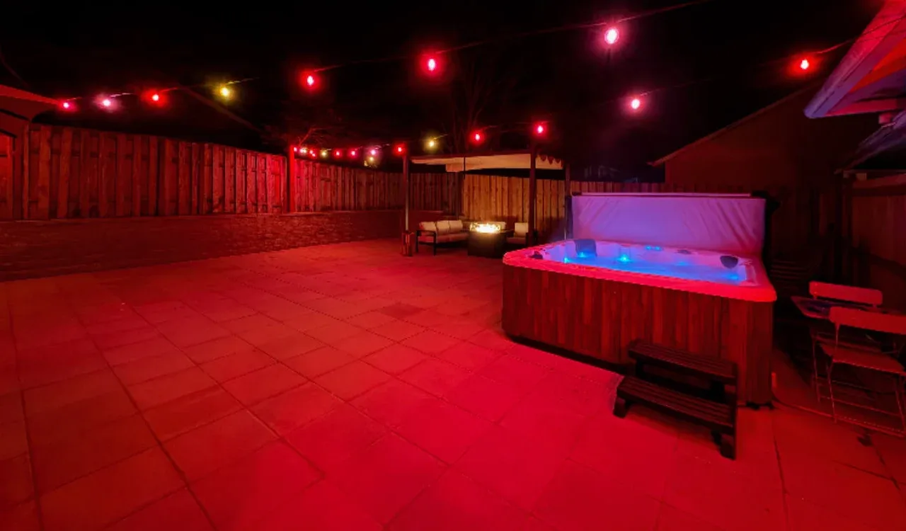An outdoor patio at night features a lit hot tub and string lights.