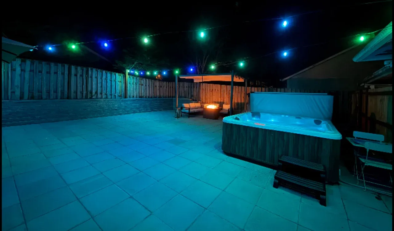 An outdoor patio with a hot tub and colorful string lights overhead.