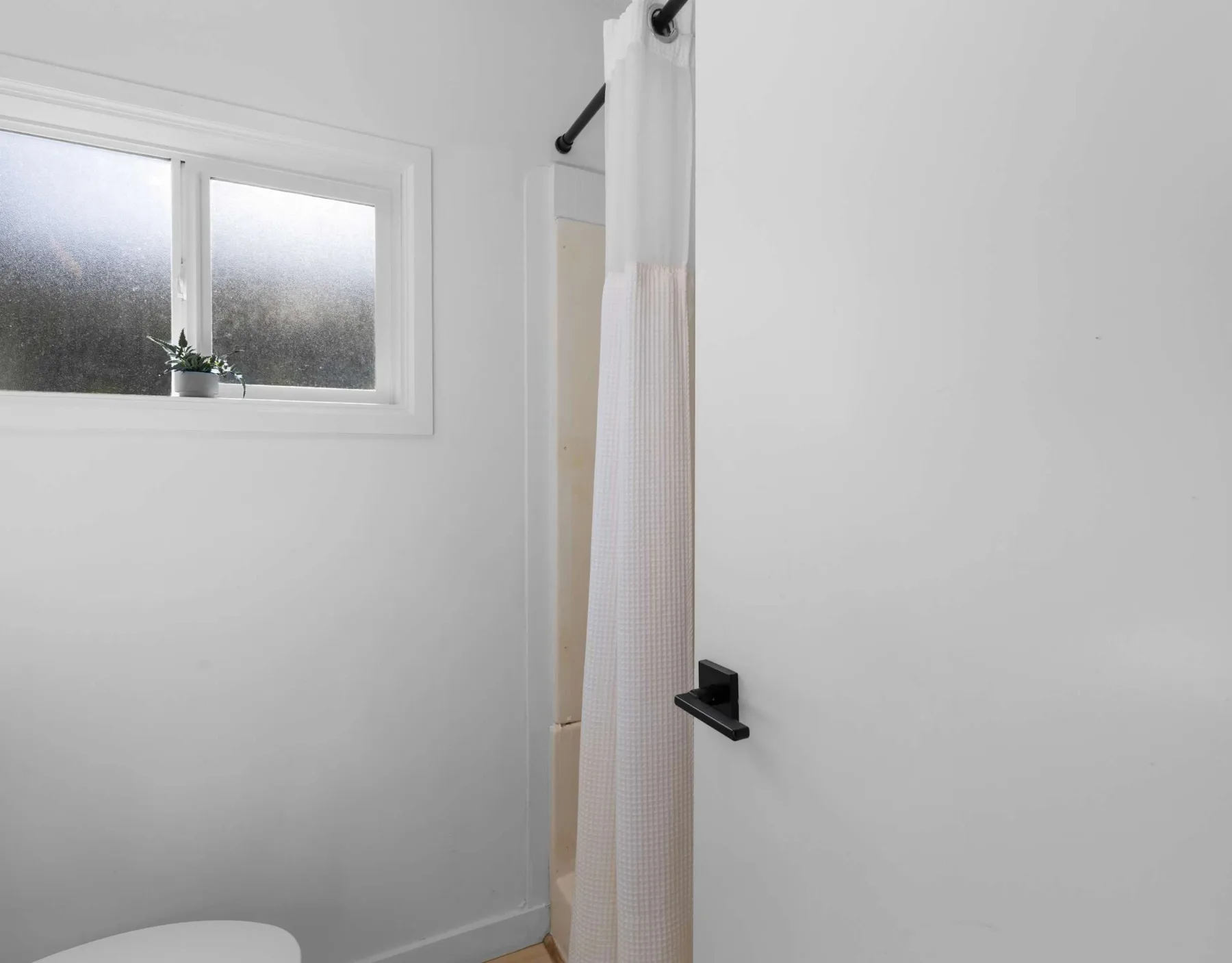 A bright bathroom with a curtained shower and a frosted window.
