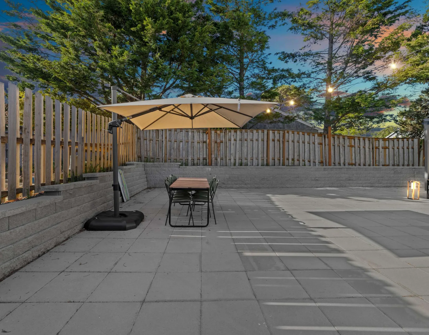A paved outdoor patio has a table, seating, and a large umbrella.
