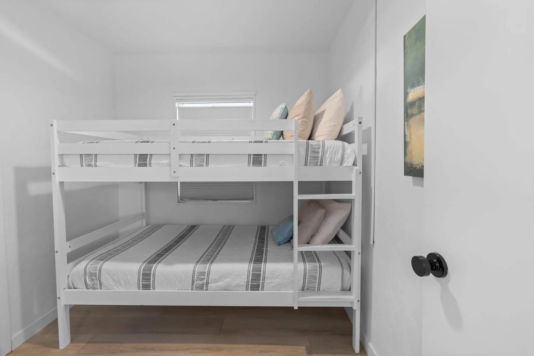 A white bunk bed with striped bedding stands in a bright bedroom.