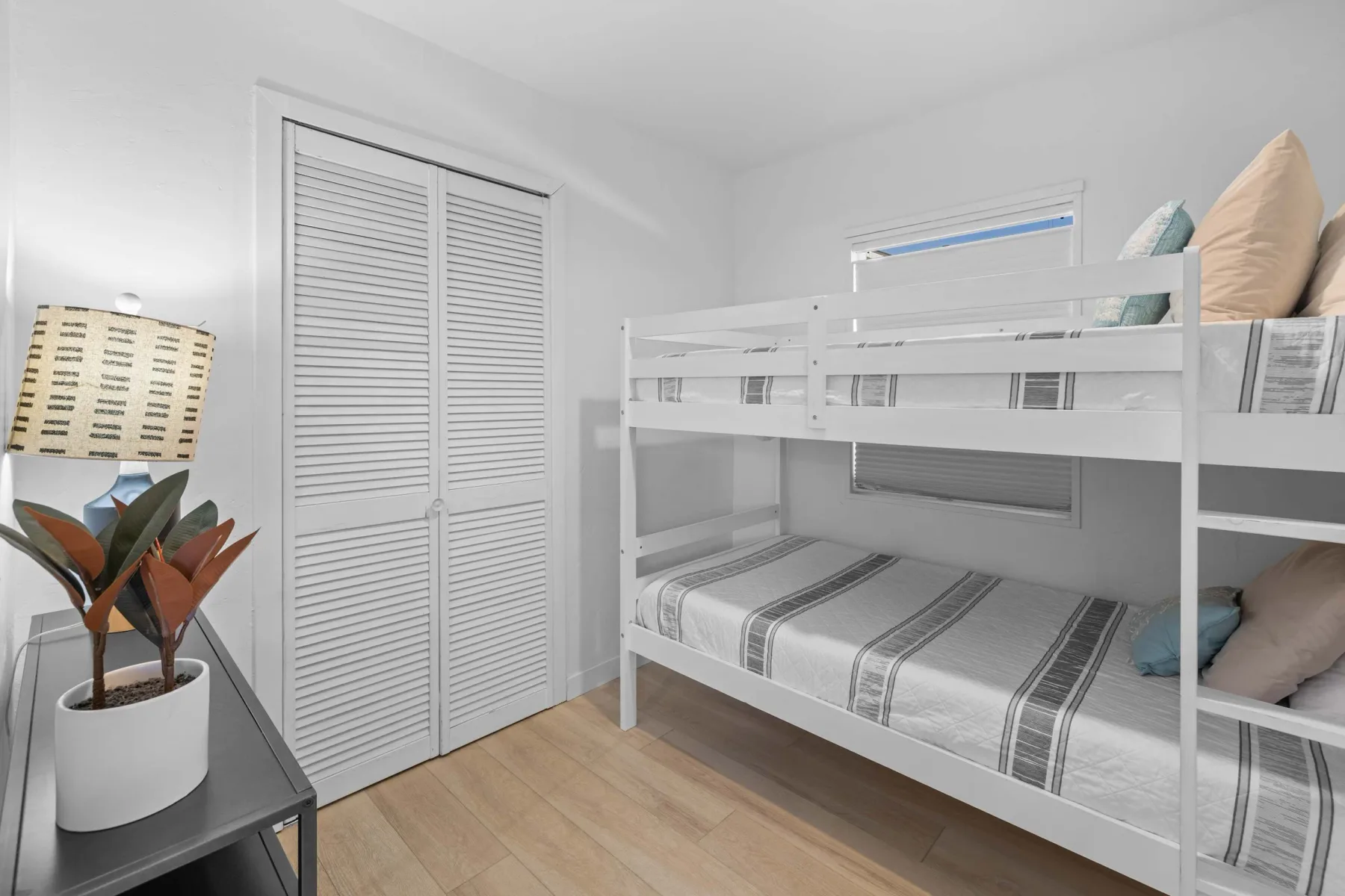 A bright bedroom with a white bunk bed and striped bedding.