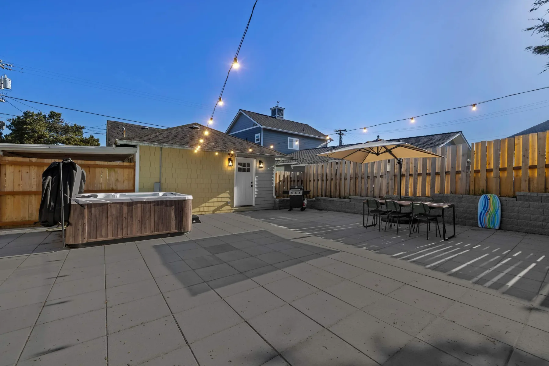 An outdoor patio with a hot tub, dining table, and string lights.