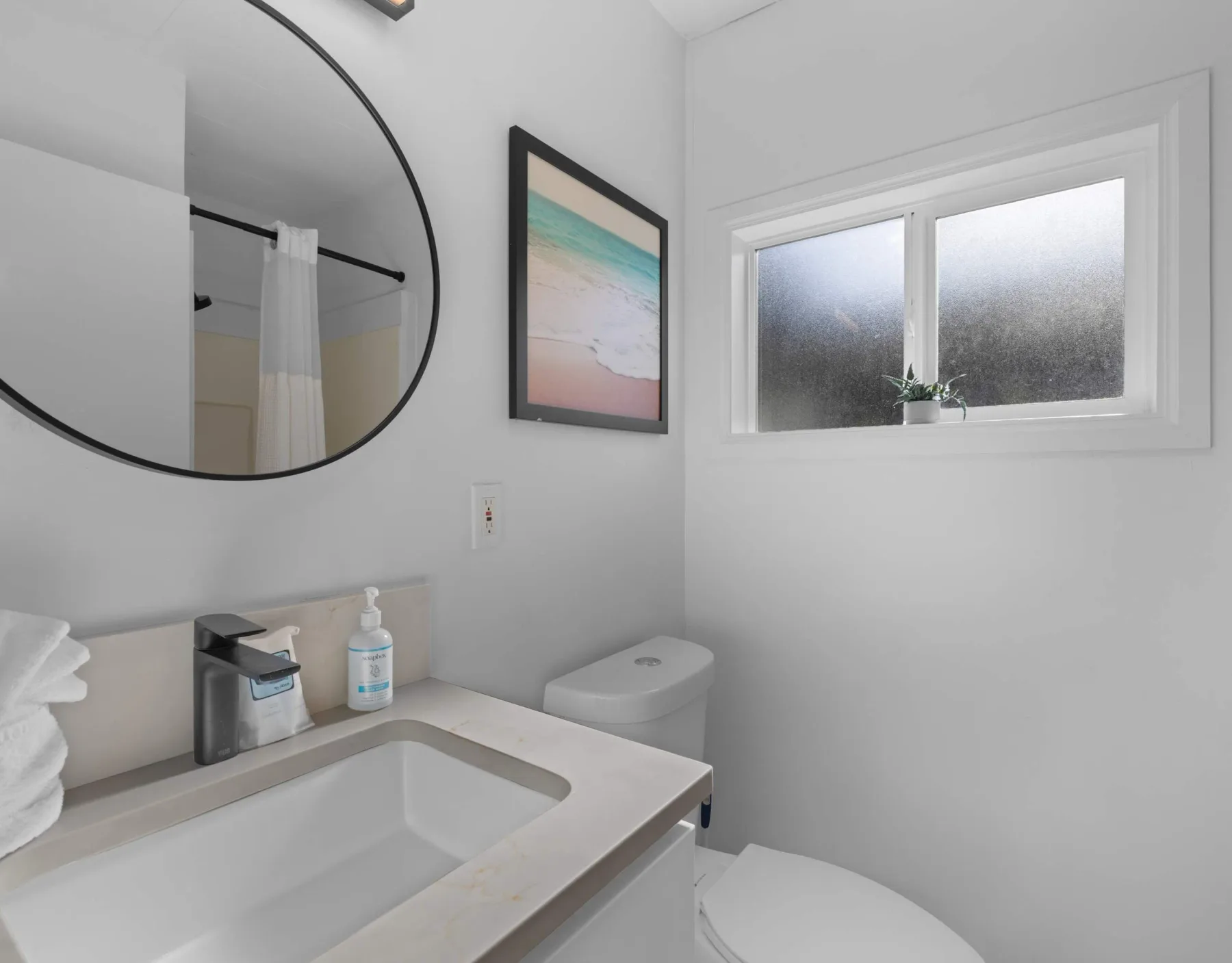 A bright bathroom with a sink, mirror, and frosted window.