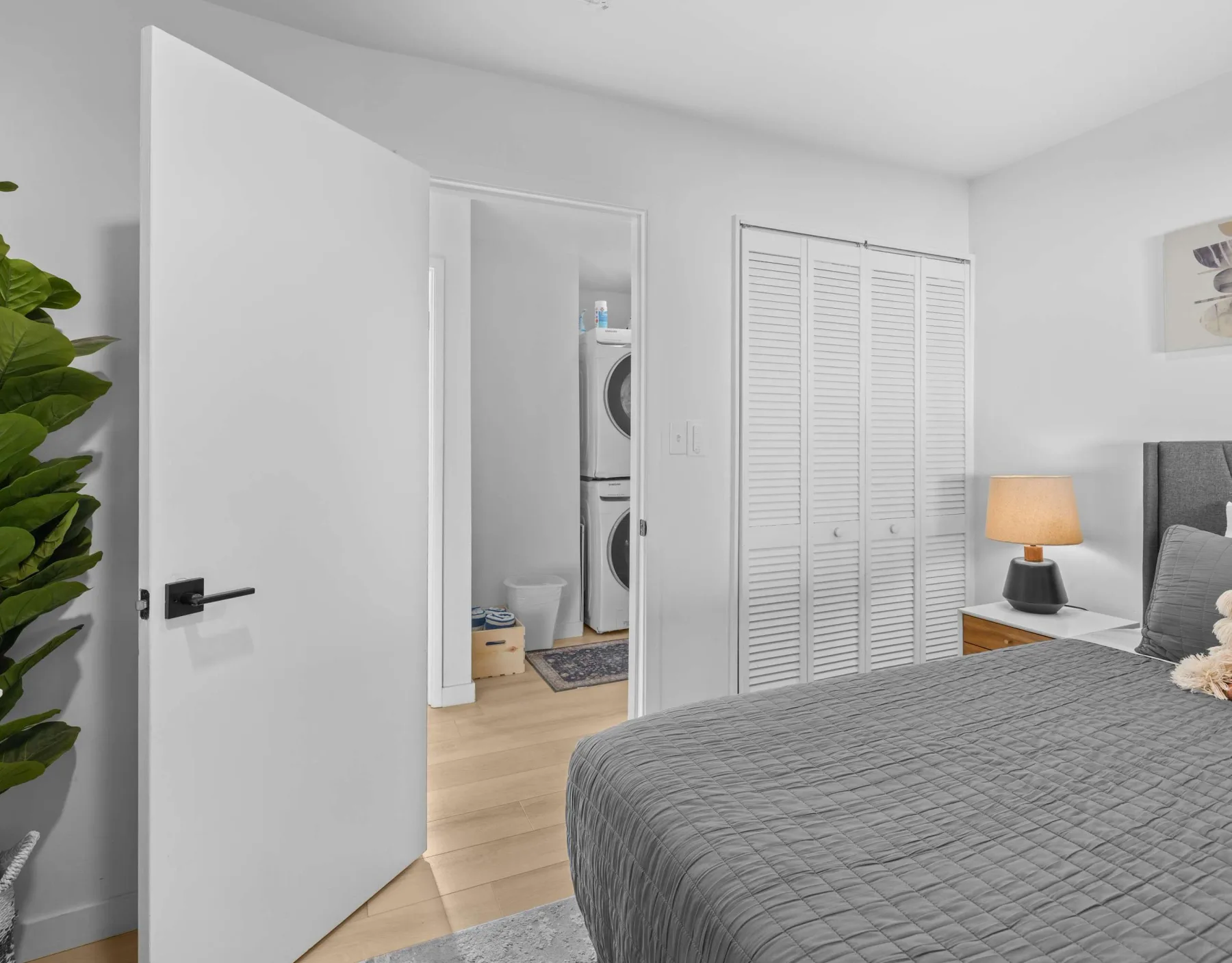 A bright bedroom with a gray bedspread, white closet doors, and an open doorway.