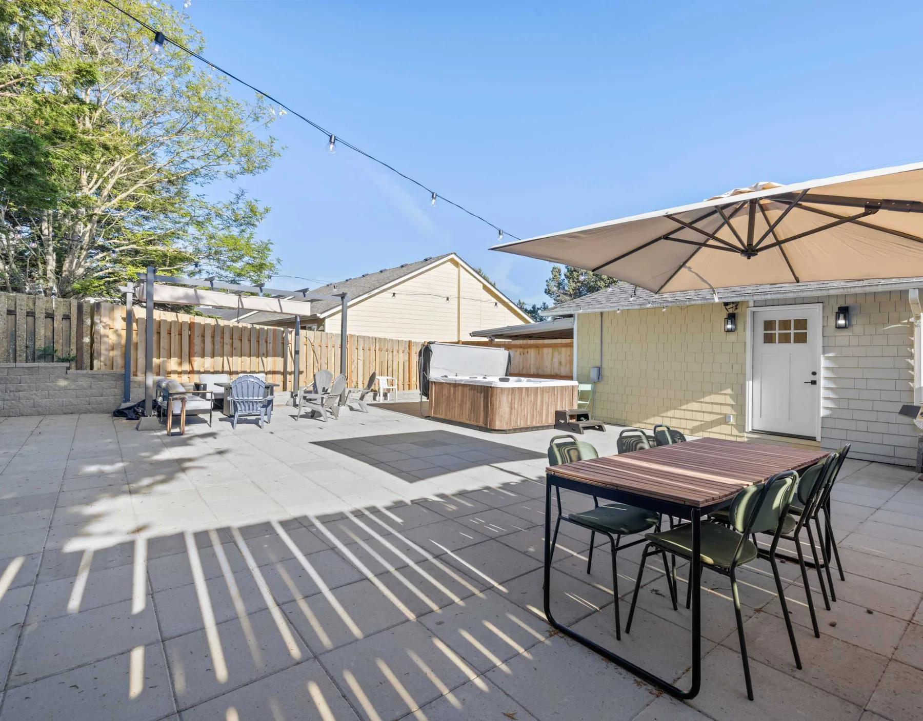 Outdoor patio with a dining table, umbrella, and hot tub beside a small building.