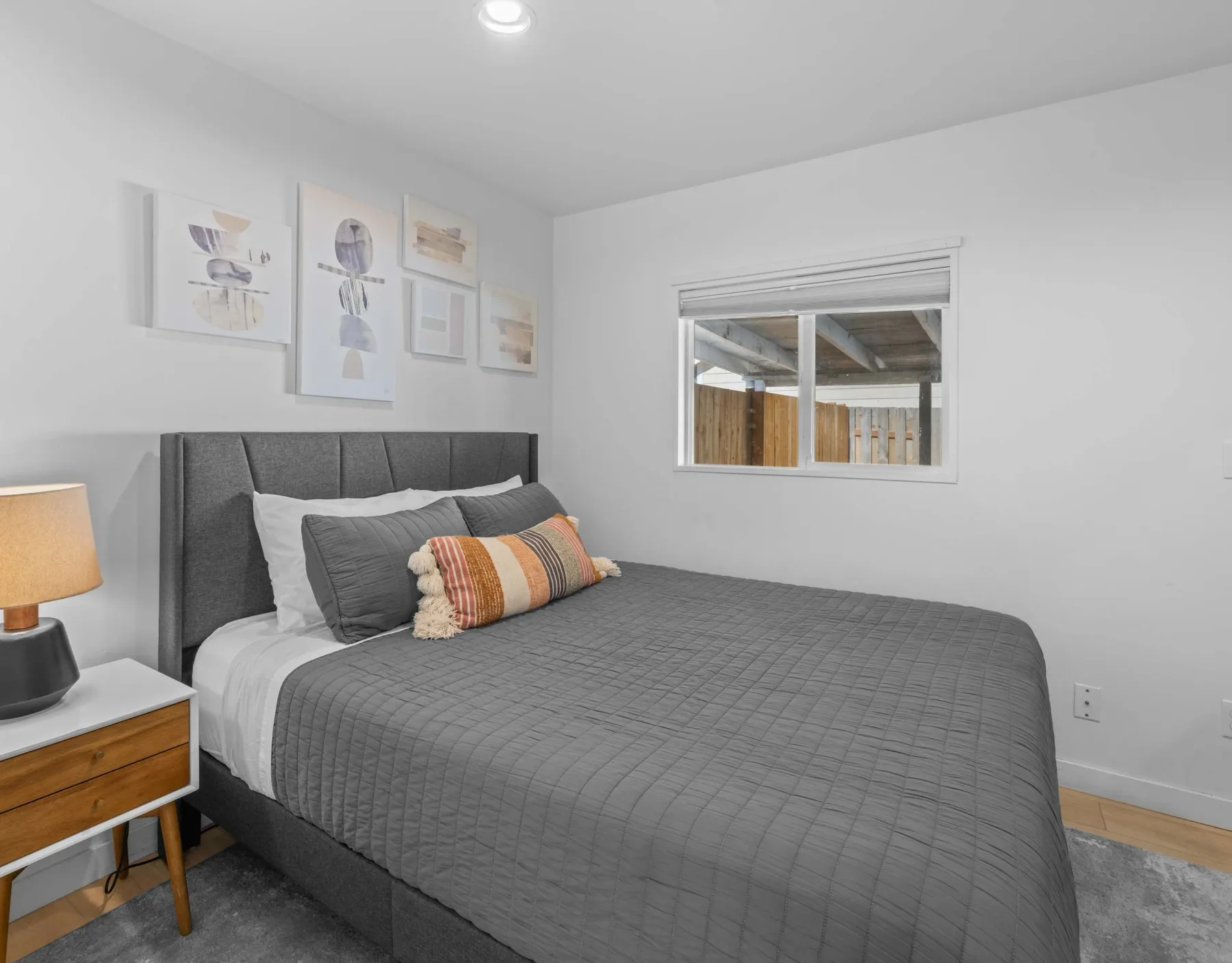 A bedroom with a bed dressed in gray bedding and framed artwork on the wall.