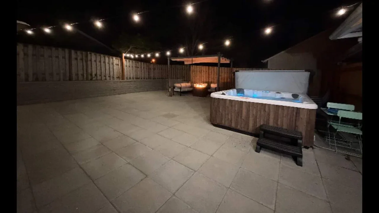 An outdoor patio at night with a lit hot tub and string lights.