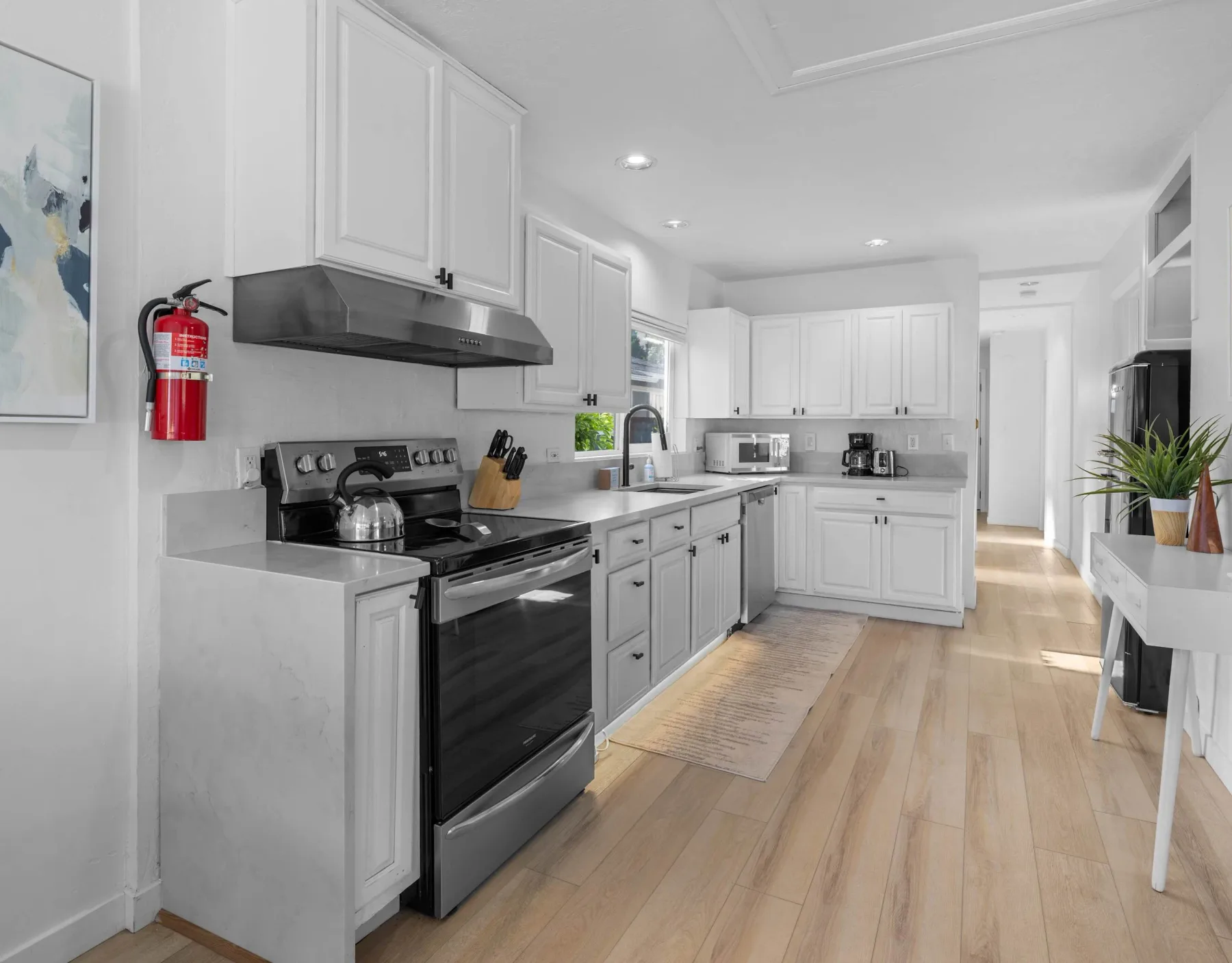 A bright white kitchen with a stove, countertops, and light wood flooring.