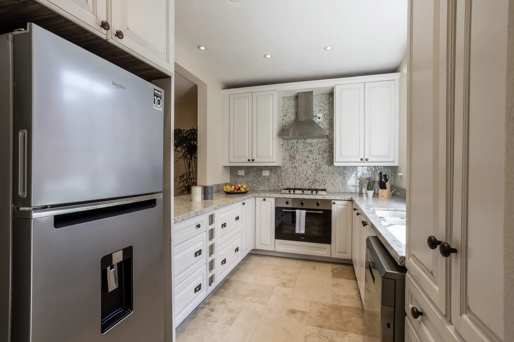 Una cocina luminosa con gabinetes blancos, electrodomésticos de acero inoxidable y un salpicadero de azulejos.