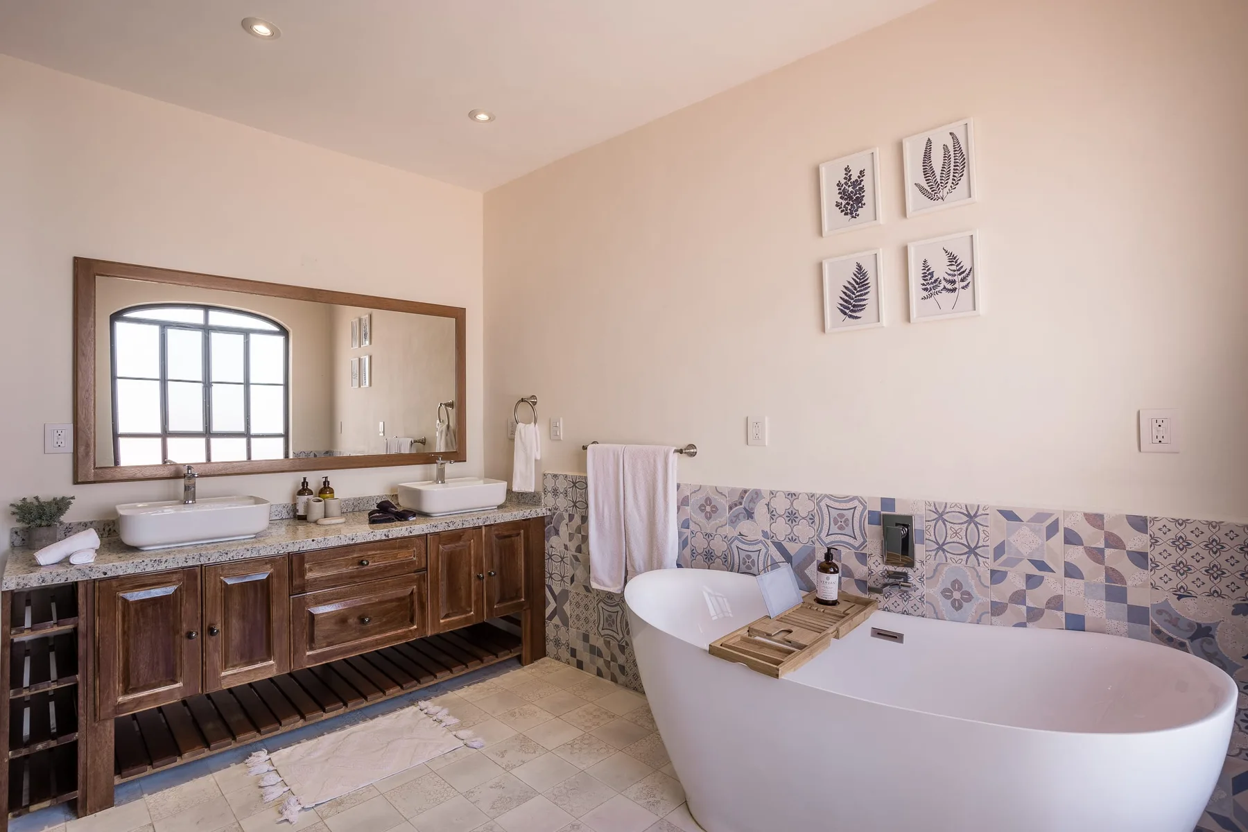 Un baño con un tocador largo, azulejos estampados y una bañera exenta.