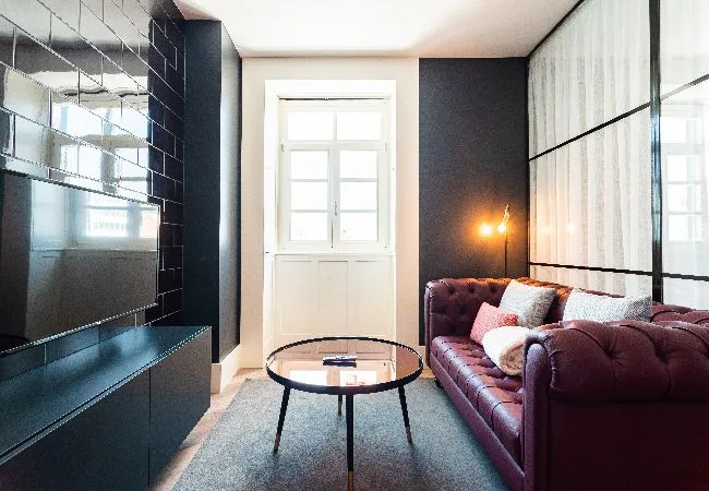 Una sala de estar con sofá burdeos, mesa de centro de vidrio y una ventana grande.