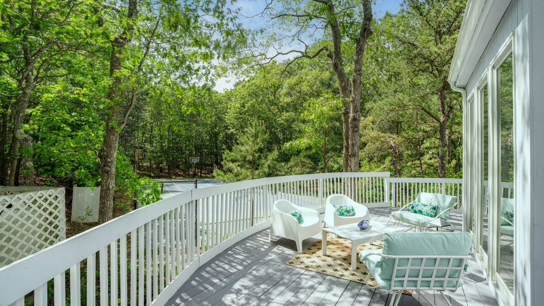 A deck with white outdoor seating overlooks a wooded area.