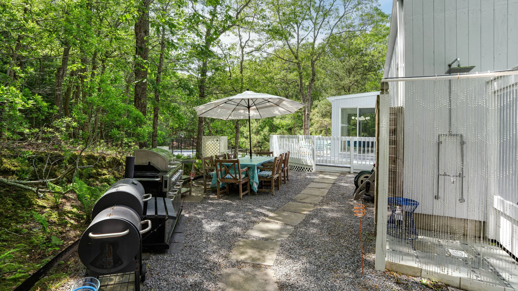 An outdoor patio with seating beneath an umbrella beside a wooded area.