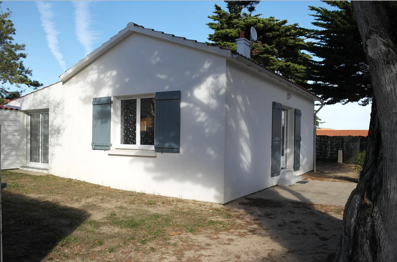 A white single-story house with blue shutters stands beside a paved walkway.
