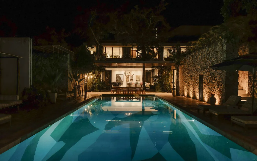 Una piscina iluminada por la noche frente a un edificio con luz.