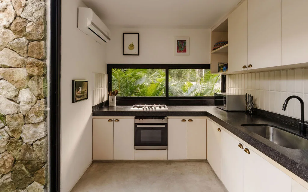 Una cocina luminosa con gabinetes blancos, encimeras oscuras y una ventana amplia.