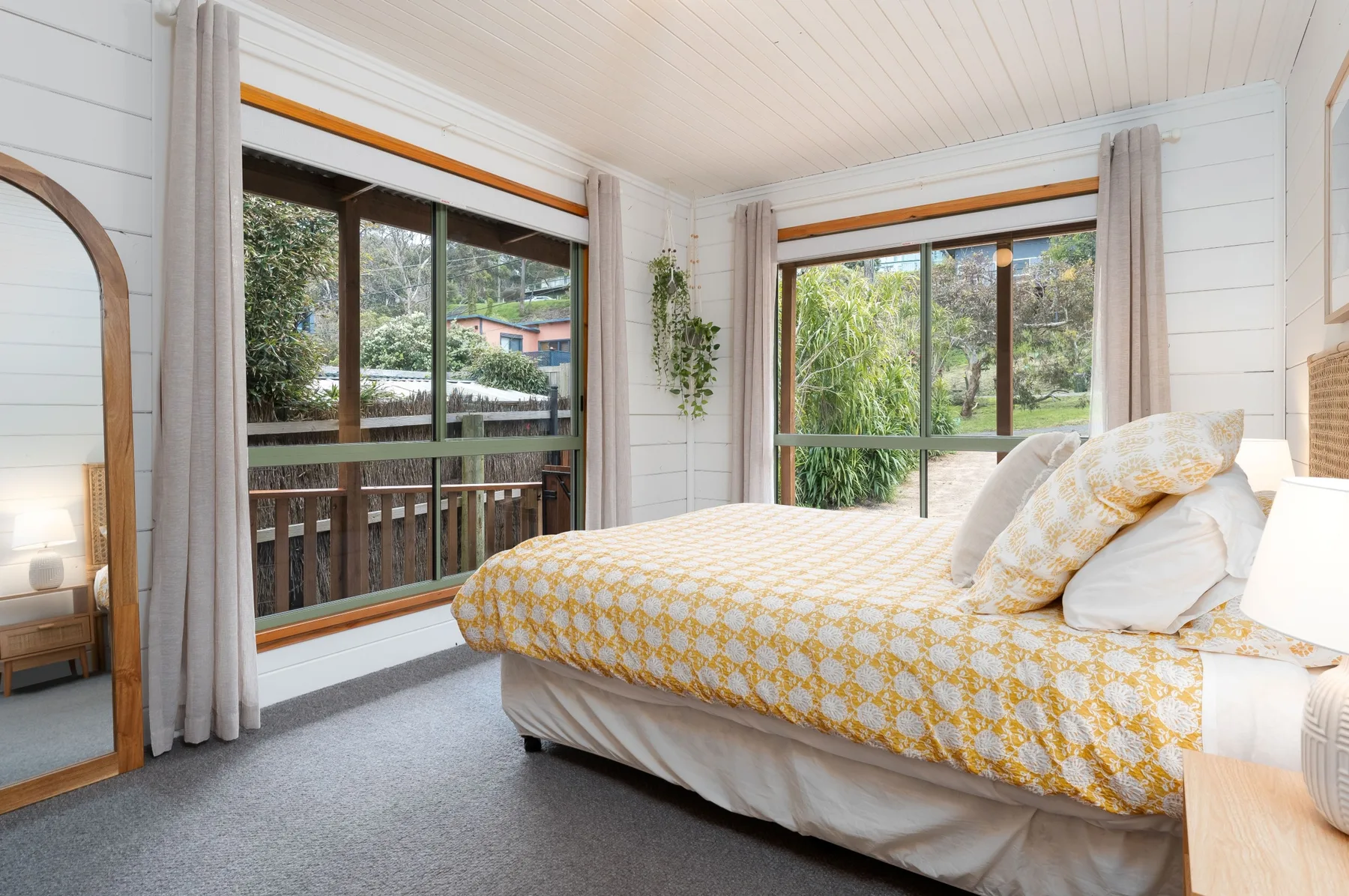 Un dormitorio con una cama junto a grandes ventanas con vistas a la vegetación.