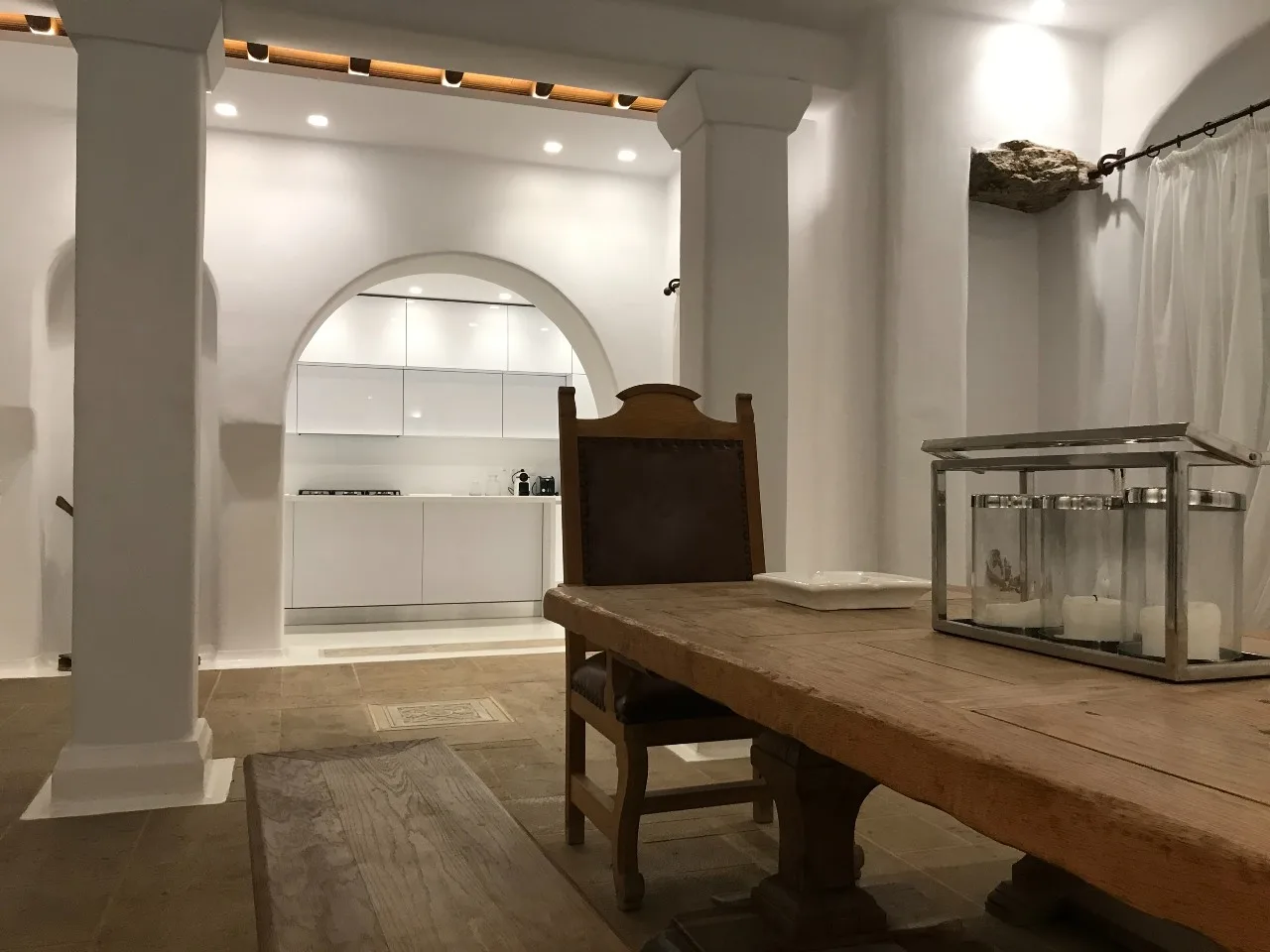 A dining area with a wooden table and a built-in kitchen visible through an arch.