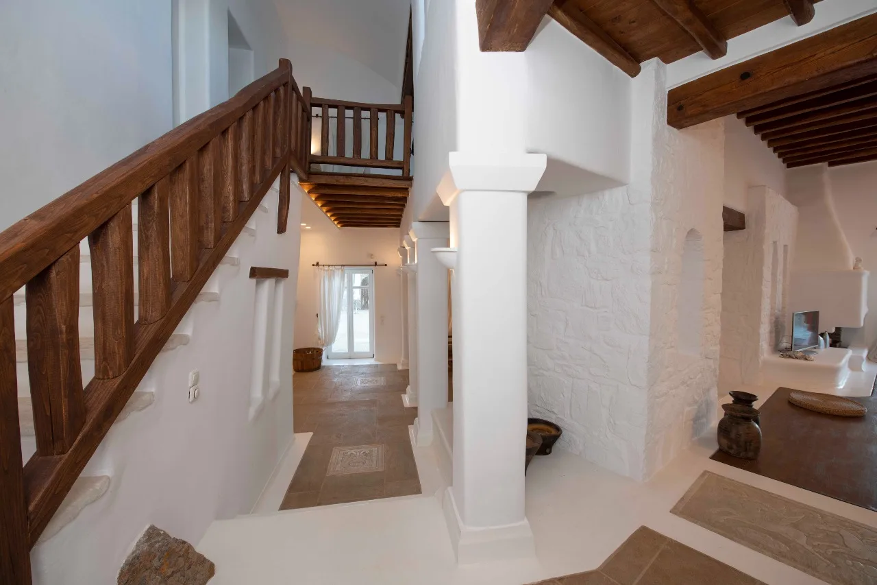 A bright interior hallway with a wooden staircase, exposed beams, and white walls.