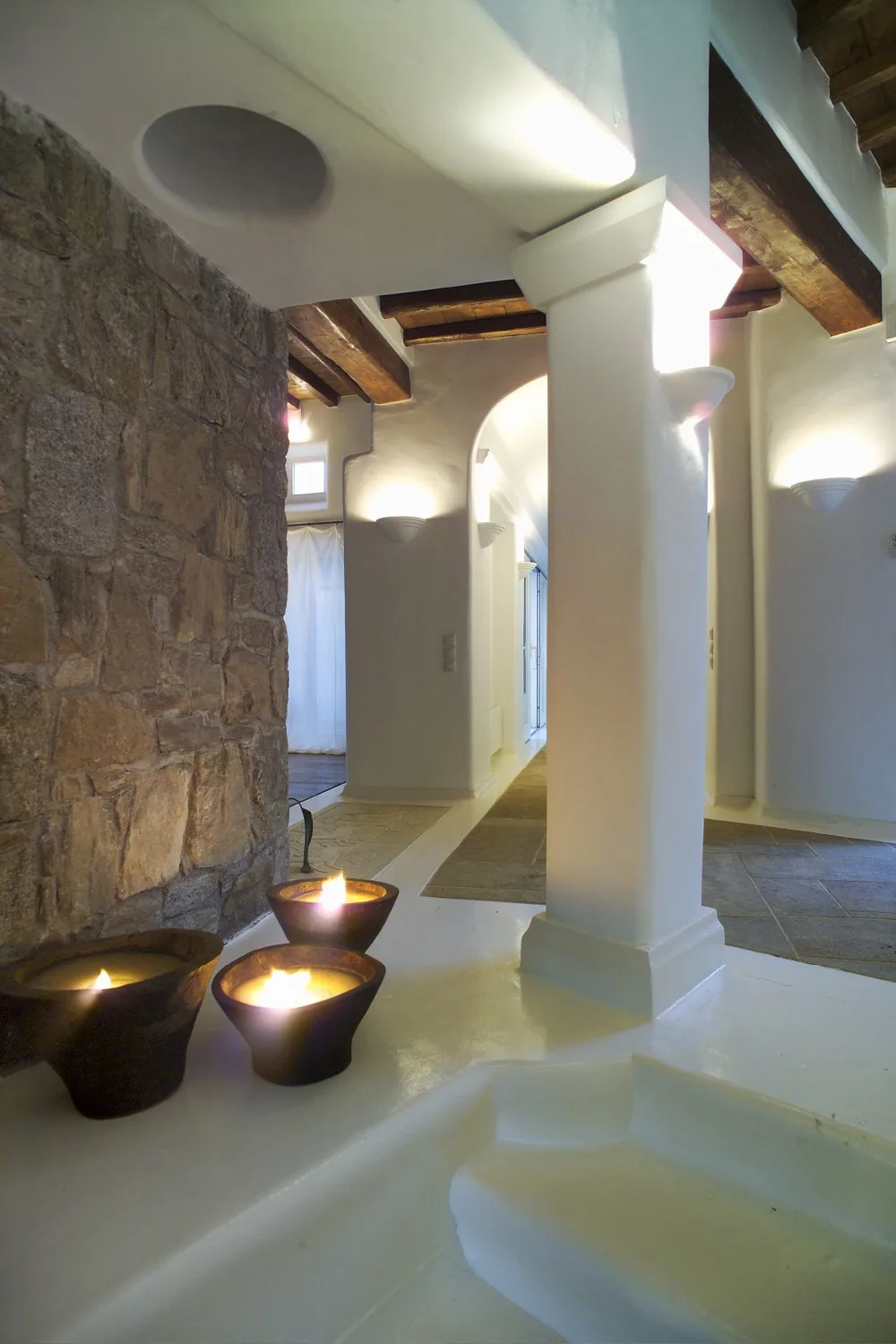 An interior hallway with white columns, exposed beams, and a stone wall.
